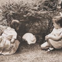 Black and white image of two children playing with a cat.