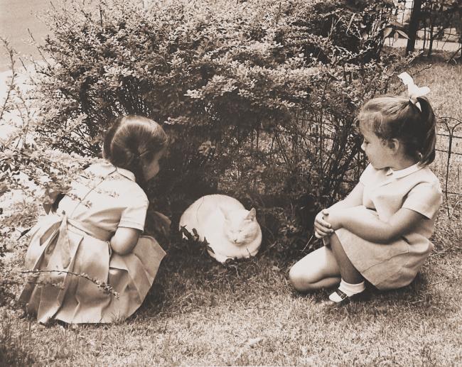 Black and white image of two children playing with a cat.